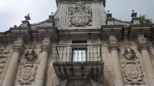Historische Steinfassade mit aufwendigen Schnitzereien und Balkon, aufgenommen aus einem niedrigen Winkel unter bewölktem Himmel
