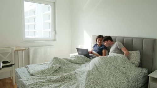 Couple in Bed Working on Laptop and Phone