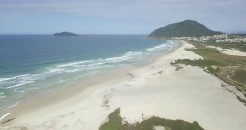 4k Aerial Tracking Shot of Paramotor Pilot Landing on the Beach with Blue Sky