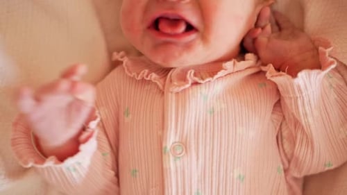 Close up of newborn baby crying in soft pink outfit