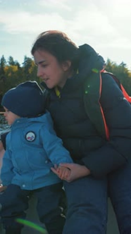 Vertical of Mother Talks to Little Son Sitting in Boat Sailing on Lake