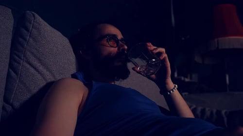 Closeup View of Young Adult Man Resting on a Sofa and Drinking Water While Watching Funny TV Program