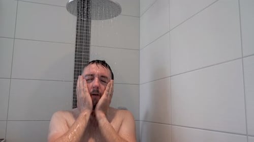 Sliding shot of naked man washing his face in the shower