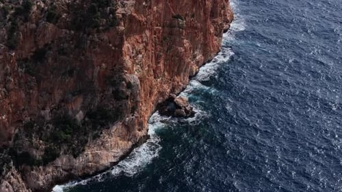 Aerial View of Intense Blue Sea with Waves Crashing Against the Majestic Red Cliffs of the Rugged