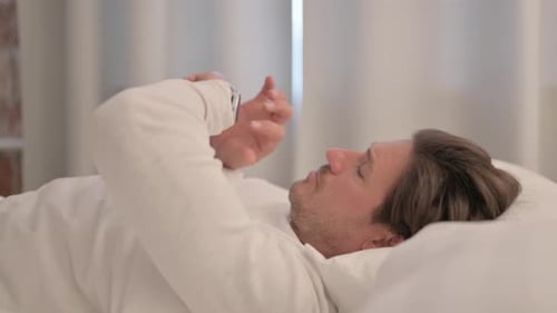 Man Lying in Bed Looking at Smartwatch