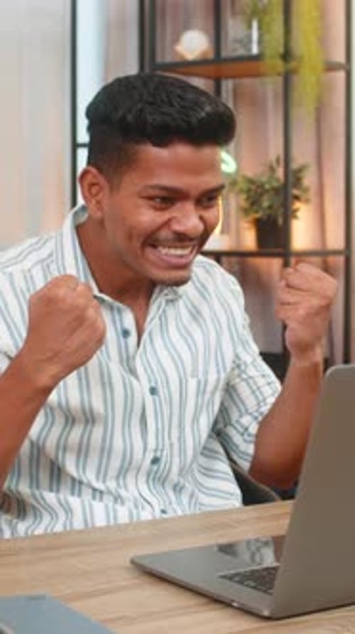 Excited Young Man Celebrating Success Using Laptop Indoors