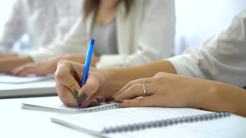 Young Adults Writing in Notebooks at Workplace