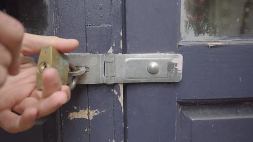 Unlocking Brass Padlock On Weathered Blue Wooden Door