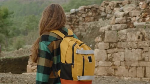 A solitary woman-traveler with a backpack walks against the backdrop of the ancient ruins.