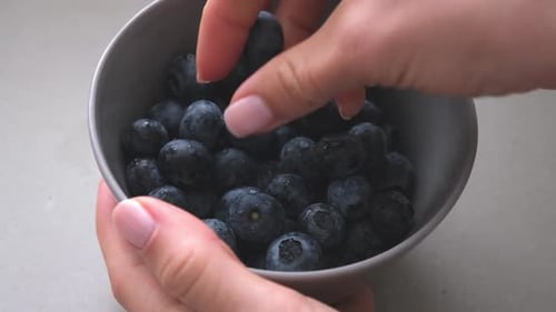 Hand Picking Fresh Blueberries from a Bowl