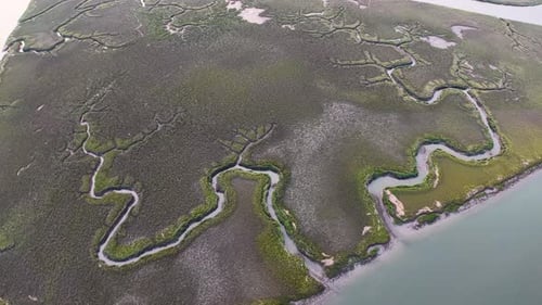 Drone footage of winding waterways through green marshland along a coastal island shoreline