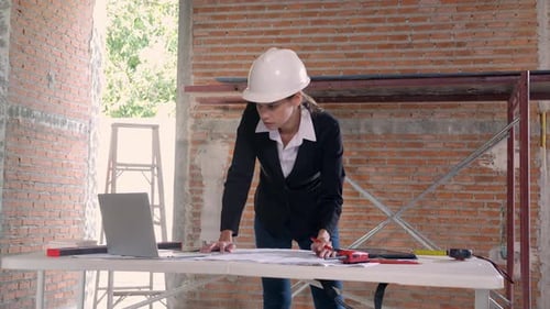 Young caucasian architect woman looking laptop and working drawing blueprint for planning building.