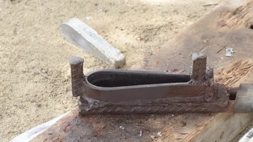 Molten metal pouring into mold on sandy ground, close-up