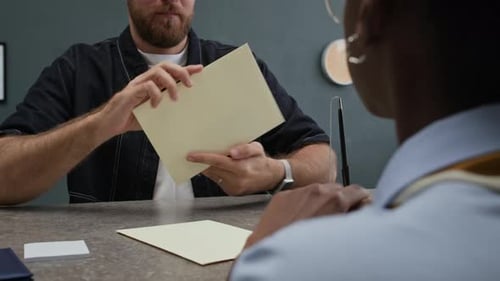 Bank Clerical Handing Envelope with Cash to Male Client