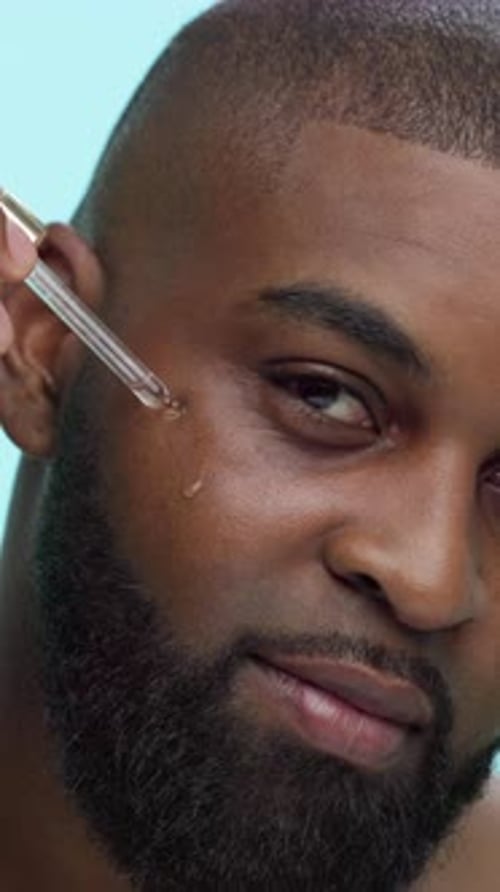Black man, face and serum with dropper in studio, skincare or cosmetic product with oil on blue