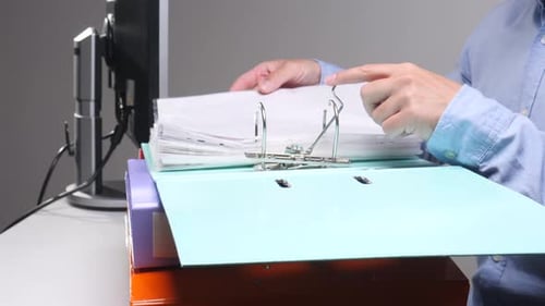 Person's Hands Organizing Documents and Files in a Light Blue Ring Binder on an Office Desk