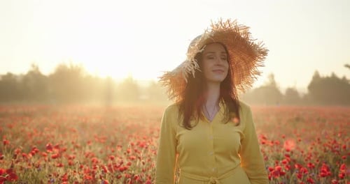 Brunette Woman in a Yellow Dress and Straw Hat in Poppy Field at Sunrise