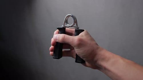 Close Up of Young Man Works with the Carpal Expander By Hand in Room with Gray Background