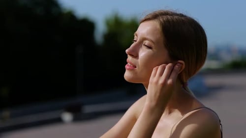 Happy Pretty Young Woman in Sports Top Sitting and Listening to Music Outdoors on the Summer Healthy