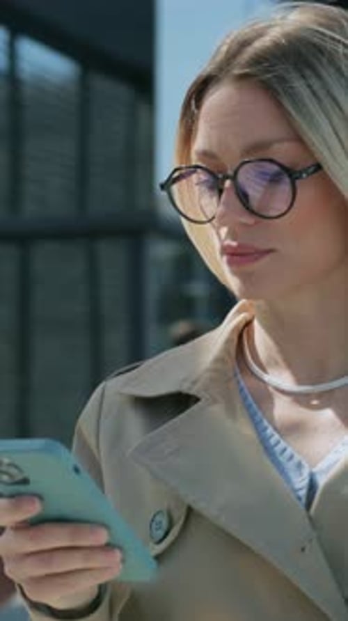 Serious Successful Attractive Businesswoman with Glasses Using Phone at Street Near Modern Building