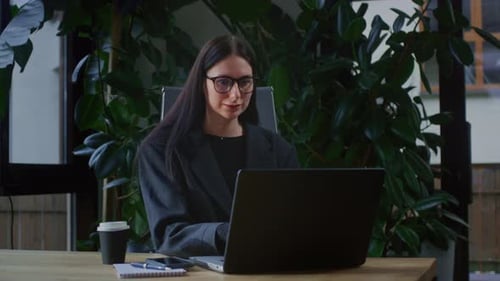 A Young Girl is Working on a Laptop in a Office with Plants Portrait of Serious Business Woman