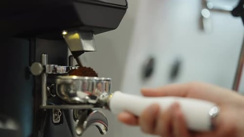 Closeup Sequence of a Barista Grinding Fresh Coffee Into a Stainless Portafilter with a Commercial