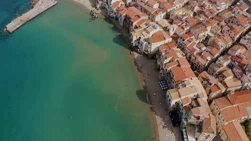 Top down aerial drone shot of Cefalu beach. Flying along the coastline of small historic town in Sic