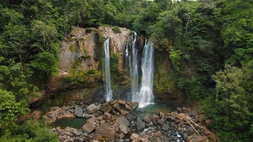 Wide view of waterfalls plunging into natural pool surrounded by dense jungle