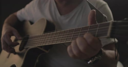 Mann spielt und spielt auf einer Akustikgitarre mit schwarzem Hintergrund und sanftem warmem Licht