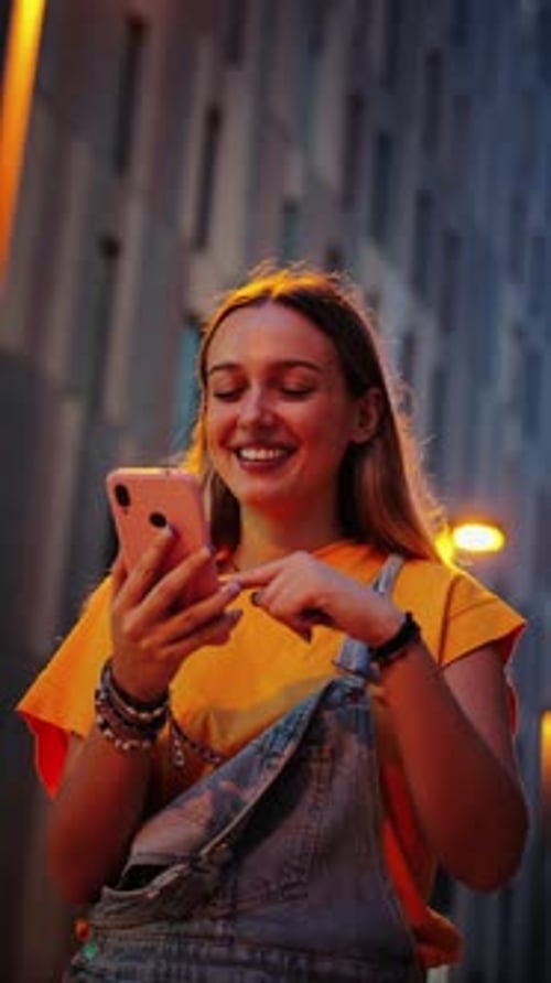 Smiling Woman Using Smartphone in Urban Setting at Night