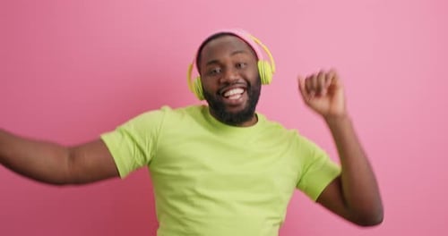 Man dances with headphones in front of pink backdrop