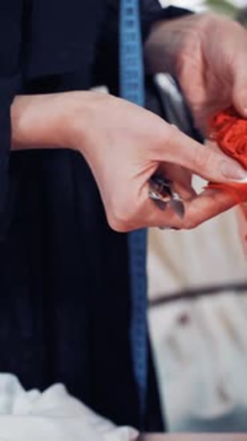 Professional dressmaker is cutting red lace with scissors with the help of a tailor in atelier.