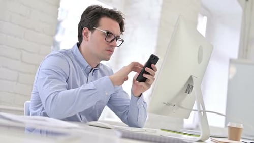 Serious Working Young Man using Smartphone in Office