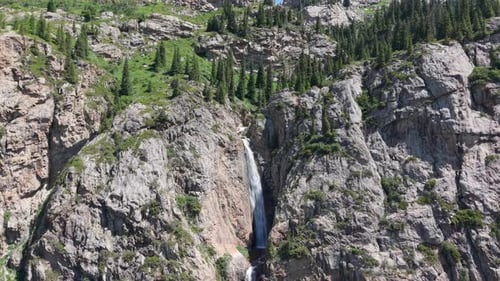 Waterfall Cascading Down Rocky Mountain Slope Surrounded By Green Vegetation