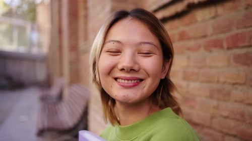 Portrait of Young Smiling Chinese Student Sitting on a Bench on Campus Looking at the Camera