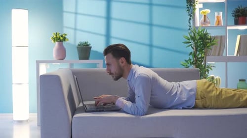 Man Lying on Sofa Typing on Laptop