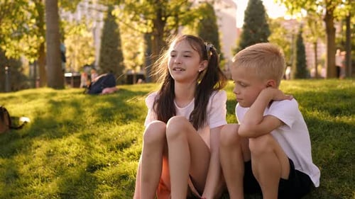 Portrait of a Happy Boy and Girl in the Park on the Grass at Sunset
