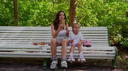 Mother and Daughter Eating Ice Cream on Bench After Skating Inline Roller in Public Park Together