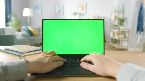 First Person Close-up Shot Man Uses Laptop with Green Mock-up Screen While Sitting at the Desk in H
