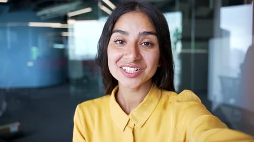 POV smiling young businesswoman talking on video call using smartphone at workplace in modern office