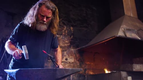 Bearded Man Blacksmith Working Metal in Dark Shop