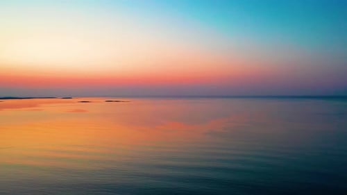 Leuchtend orangefarbener Sonnenaufgang am Meer mit Farben, die sich über plätschernden Wasserwellen spiegeln. Buntes Orange, Rot