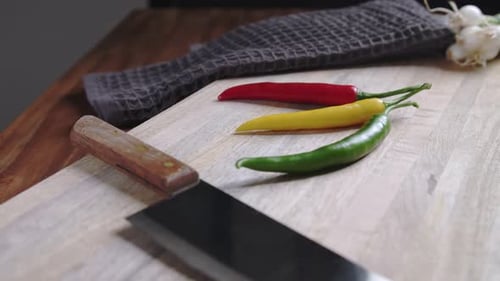 Camera pulls back from colourful chili peppers on cutting board to reveal bunch of green onions.