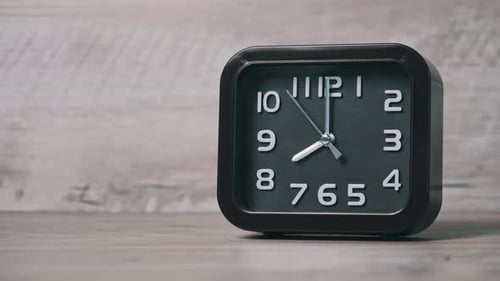 Eine quadratische Pfeiluhr auf einem Holztisch zeigt die Uhrzeit 8 Stunden an