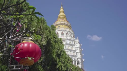 Circle pan reveals pagoda behind bush in Kek Lok Si temple, sunny day