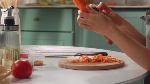 Woman peels carrot at kitchen table for cooking