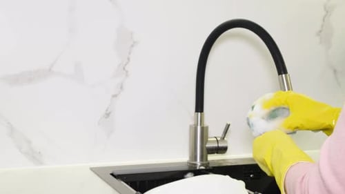 A Woman's Hand Washes a White Plate with Dishwashing Liquid Dirty Dishes in the Kitchen at Home