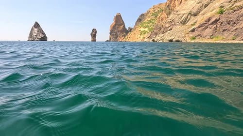 Sea Water Surface Camera Flies Over the Calm Azure Sea with Volcanic Rocky Shores on Background