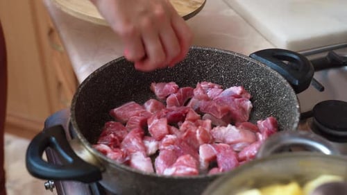 Hands placing raw meat cubes in a frying pan