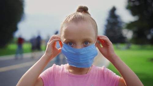Portrait of Beautiful Girl Putting Medical Mask on Face in Garden. Young